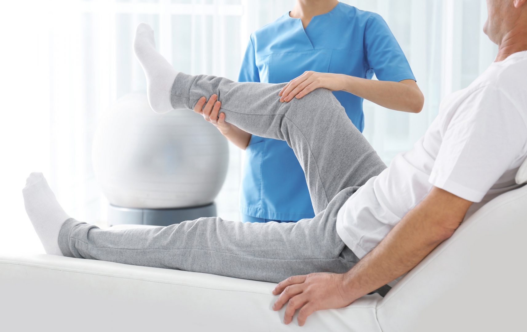 Eine Physiotherapeutin unterstützt einen Patienten bei einer Bewegungsübung für das Knie.